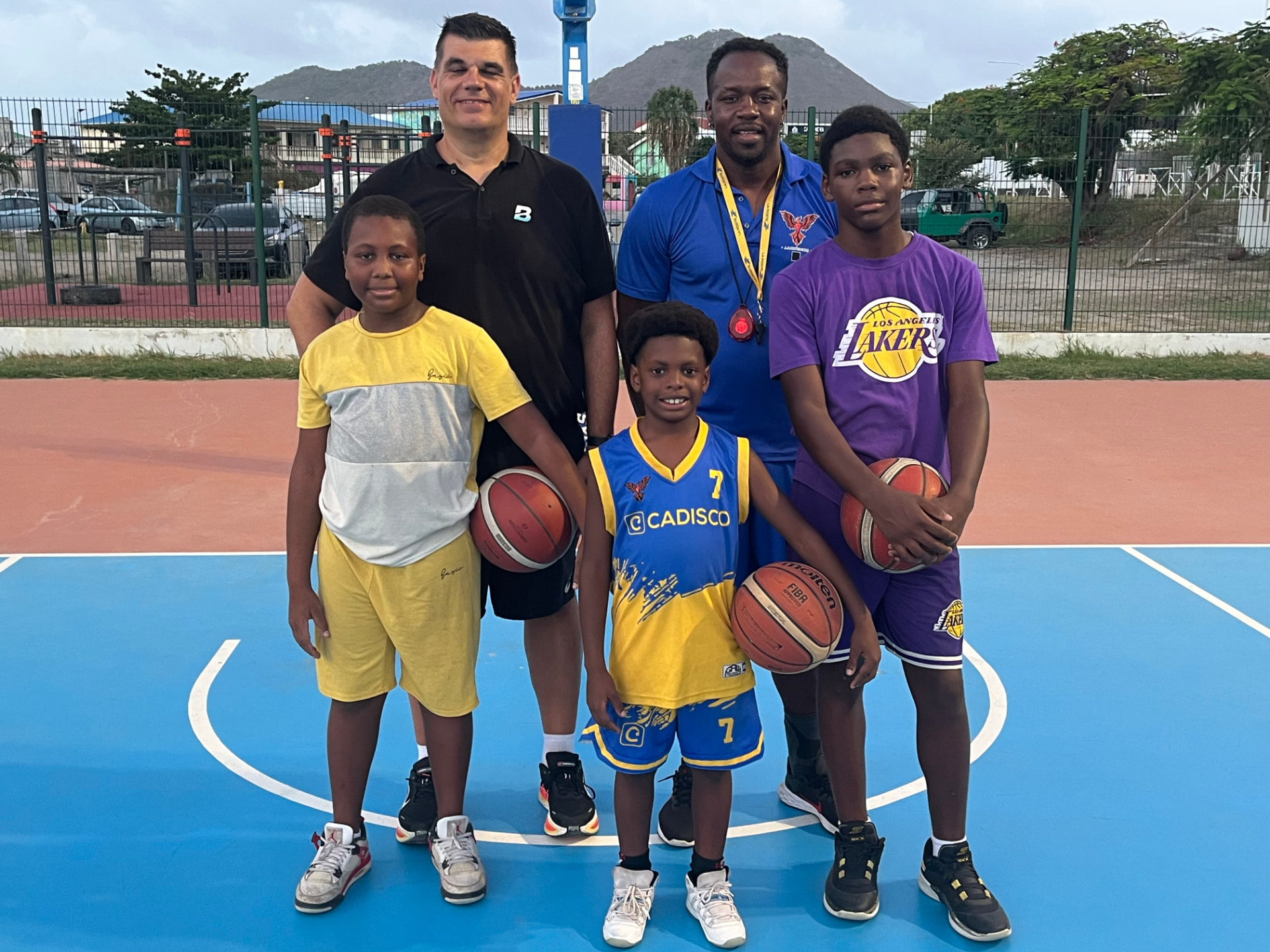Jean Pierre et un coach entourés de jeunes joueurs sur un playground des Antilles
